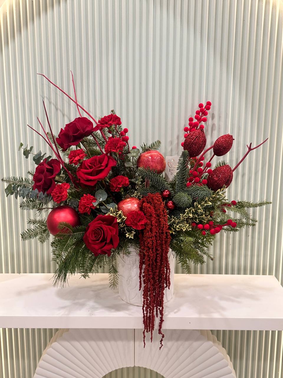 Elegant red Christmas floral arrangement with roses, ornaments, and winter greenery
