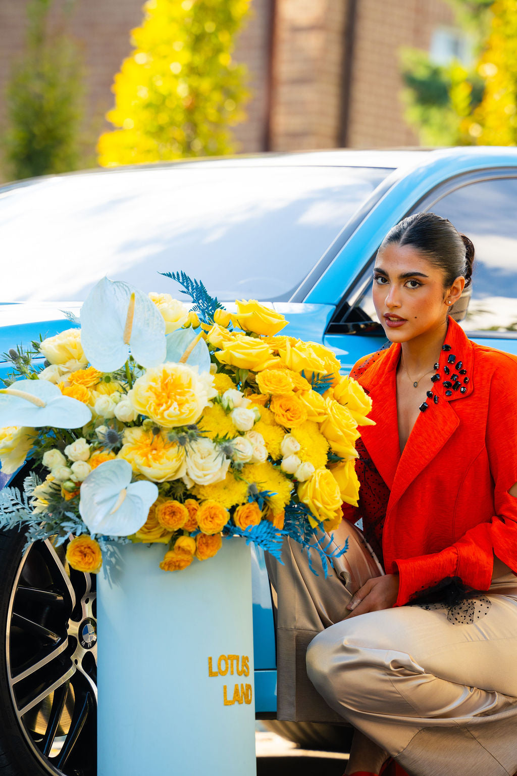Luxury yellow and white floral arrangement in a Lotus Land signature box beside a blue BMW luxury car , elegant, modern, and high-end floral design by Lotus Land Boutique