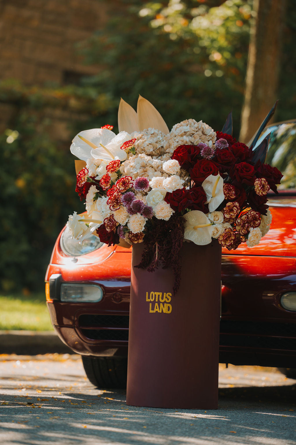 Luxury oversized floral arrangement by Lotus Land Boutique featuring premium red, white, and champagne blooms displayed beside a classic Porsche elegant, high-end floral design for modern celebrations