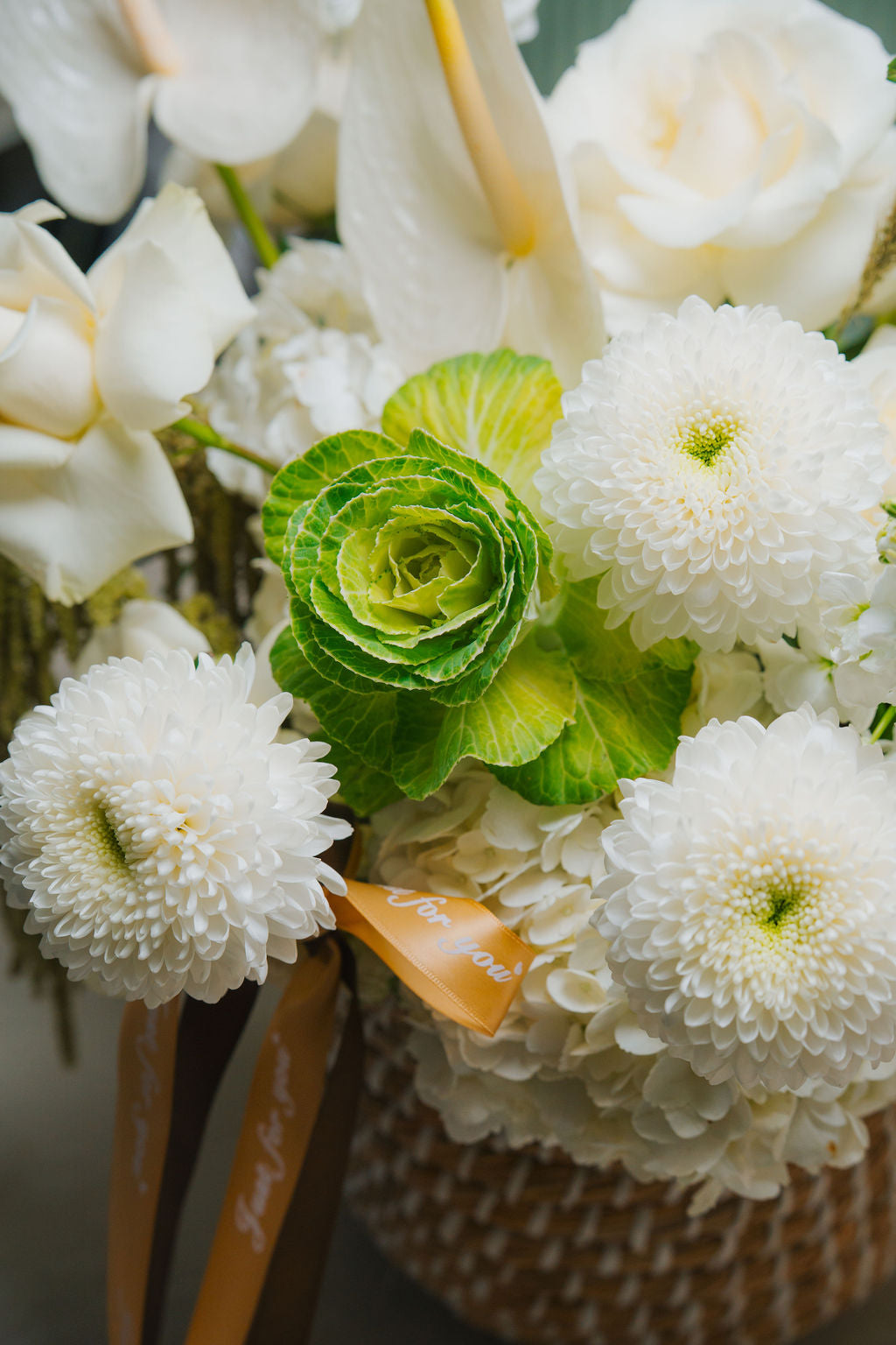Luxury white floral basket with anthurium, roses, and textured greenery in a woven basket