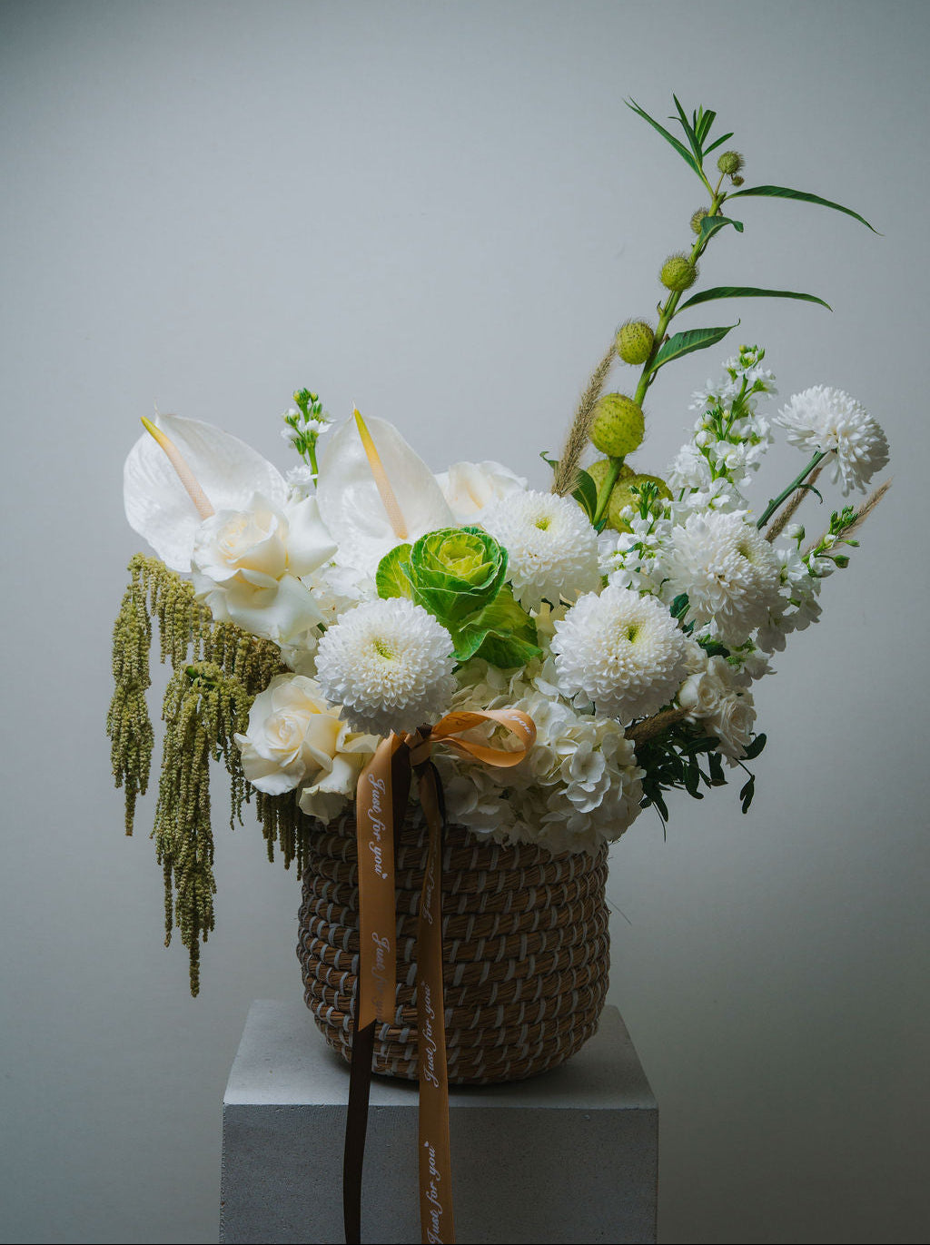 Luxury white floral basket with anthurium, roses, and textured greenery in a woven basket