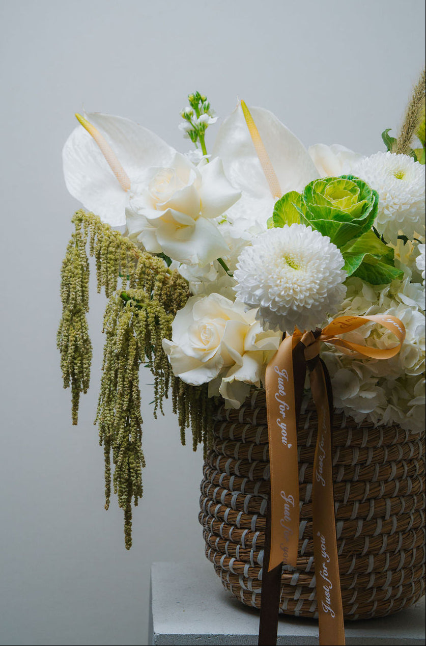 Luxury white floral basket with anthurium, roses, and textured greenery in a woven basket