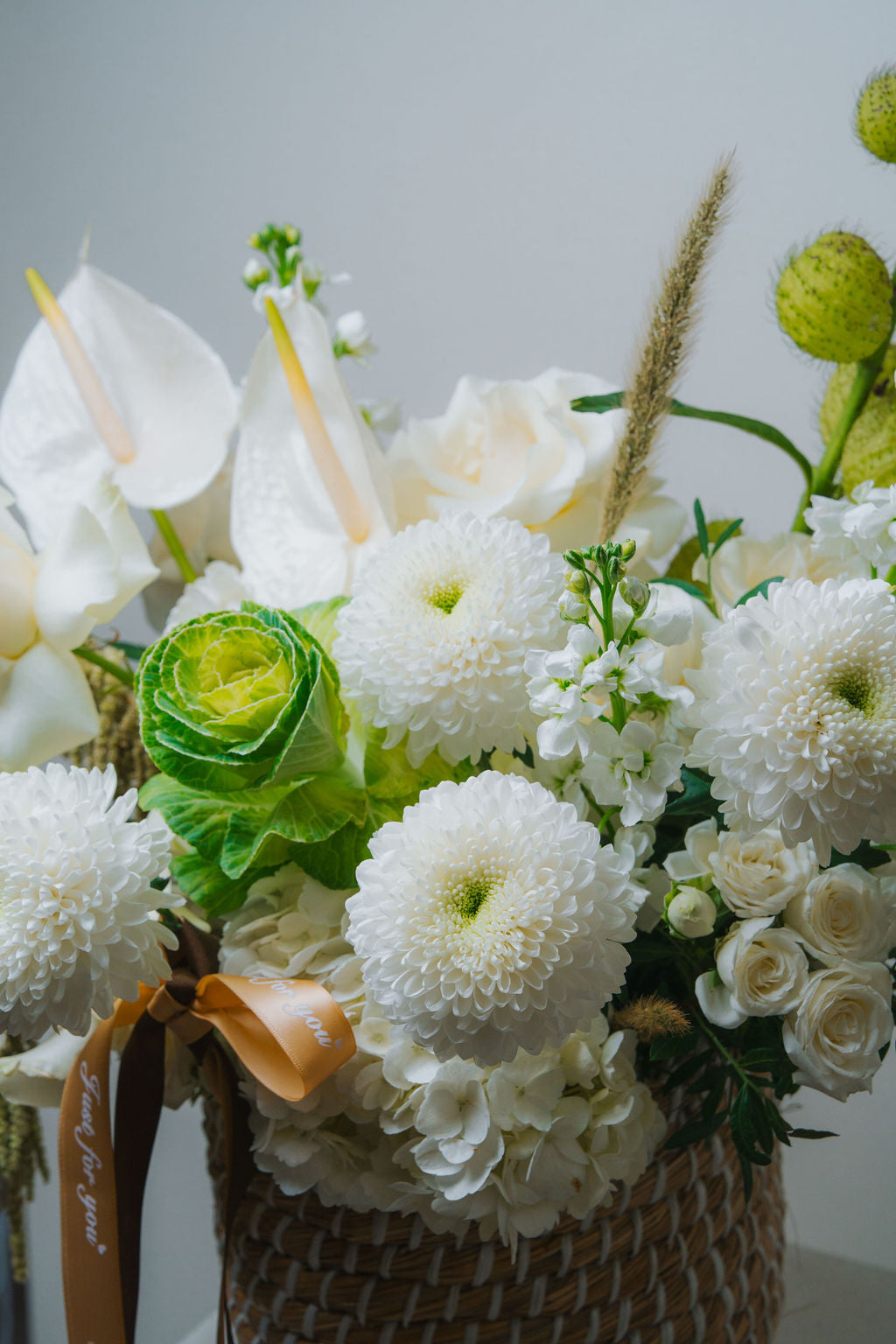 Luxury white floral basket with anthurium, roses, and textured greenery in a woven basket