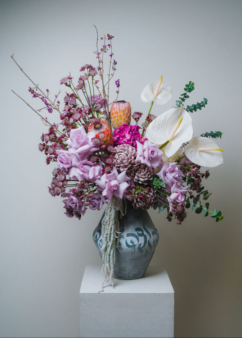 Luxury pastel floral arrangement with blush roses, white anthurium, and protea in a ceramic vase