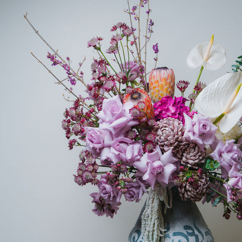 Luxury pastel floral arrangement with blush roses, white anthurium, and protea in a ceramic vase
