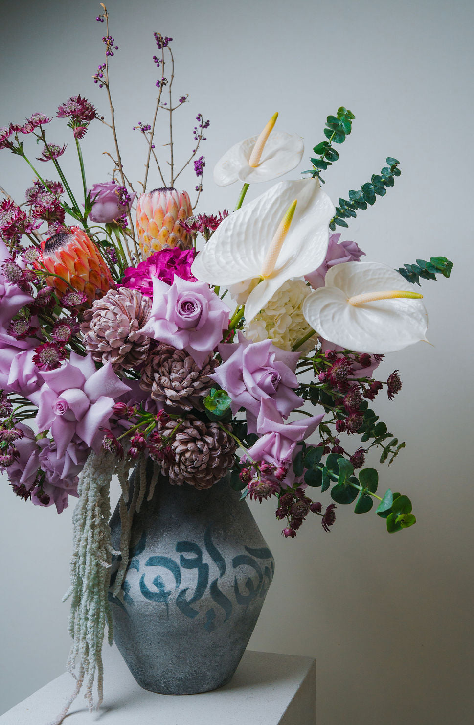 Luxury pastel floral arrangement with blush roses, white anthurium, and protea in a ceramic vase