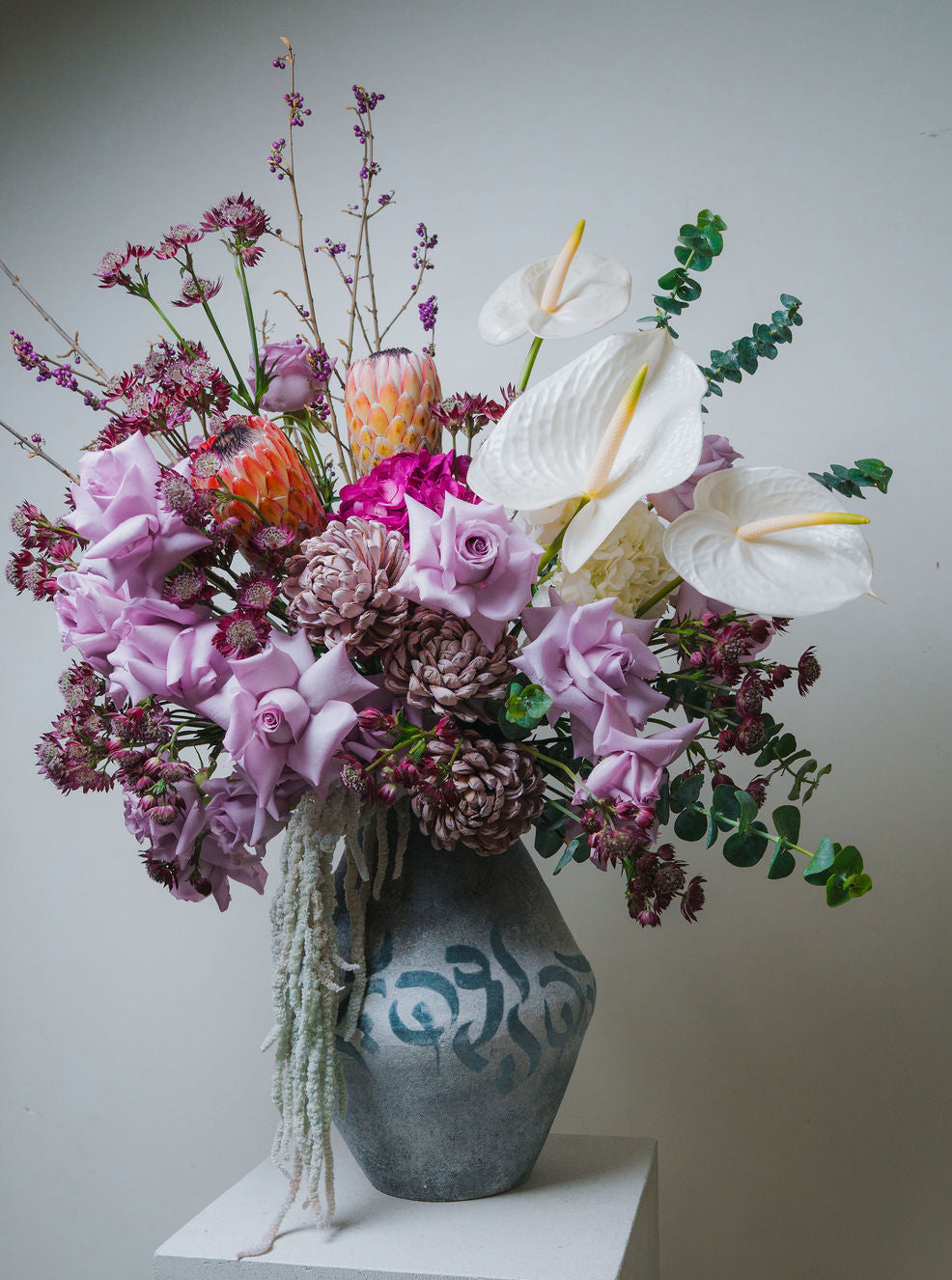 Luxury pastel floral arrangement with blush roses, white anthurium, and protea in a ceramic vase