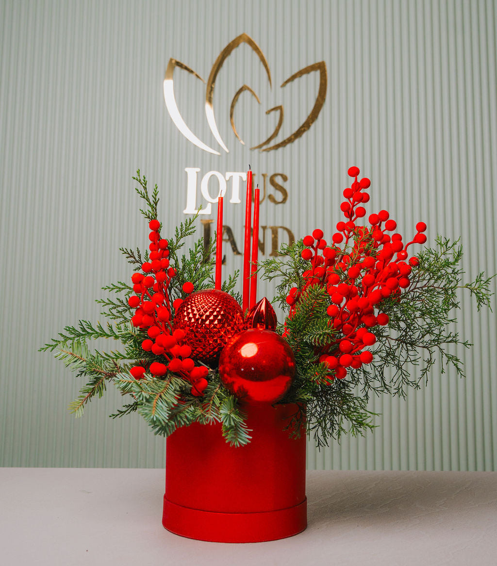 Decorative flower arrangement with red berries and ornaments in a red box  and red candle